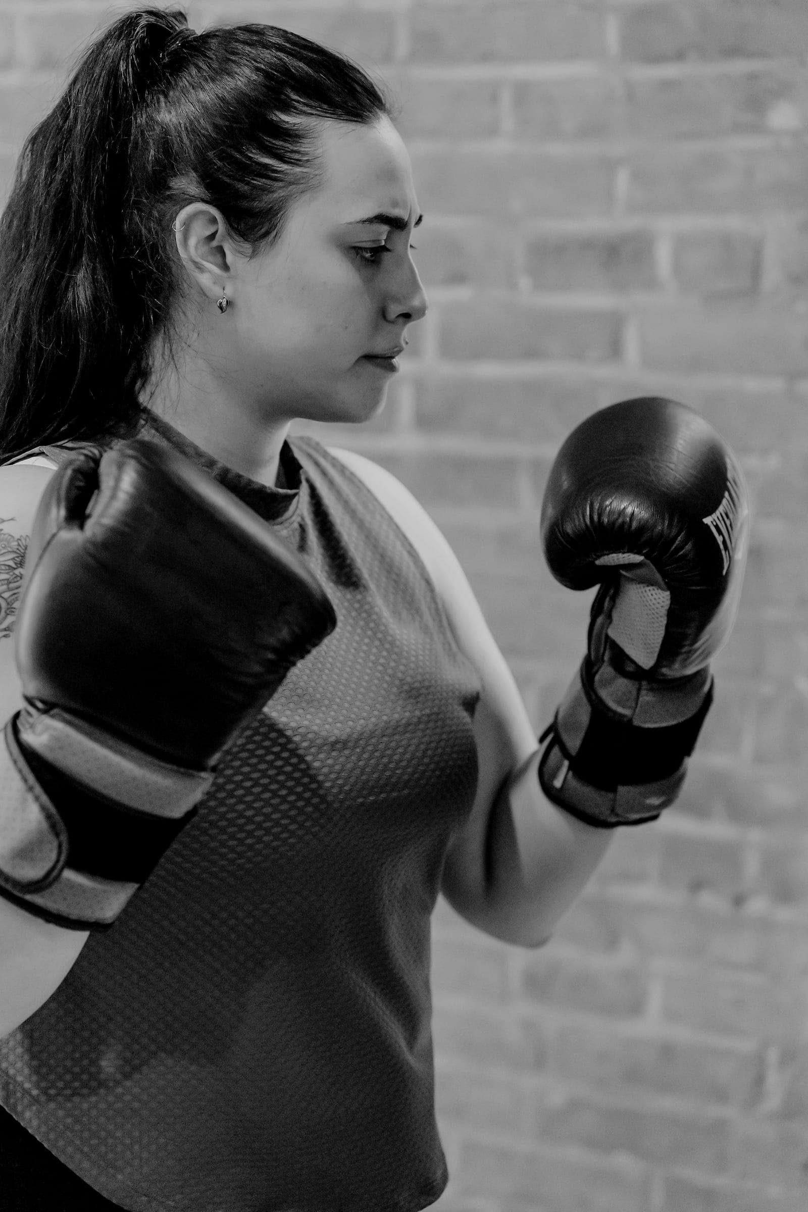 A boxer holds her guard up in front of a brick wall.