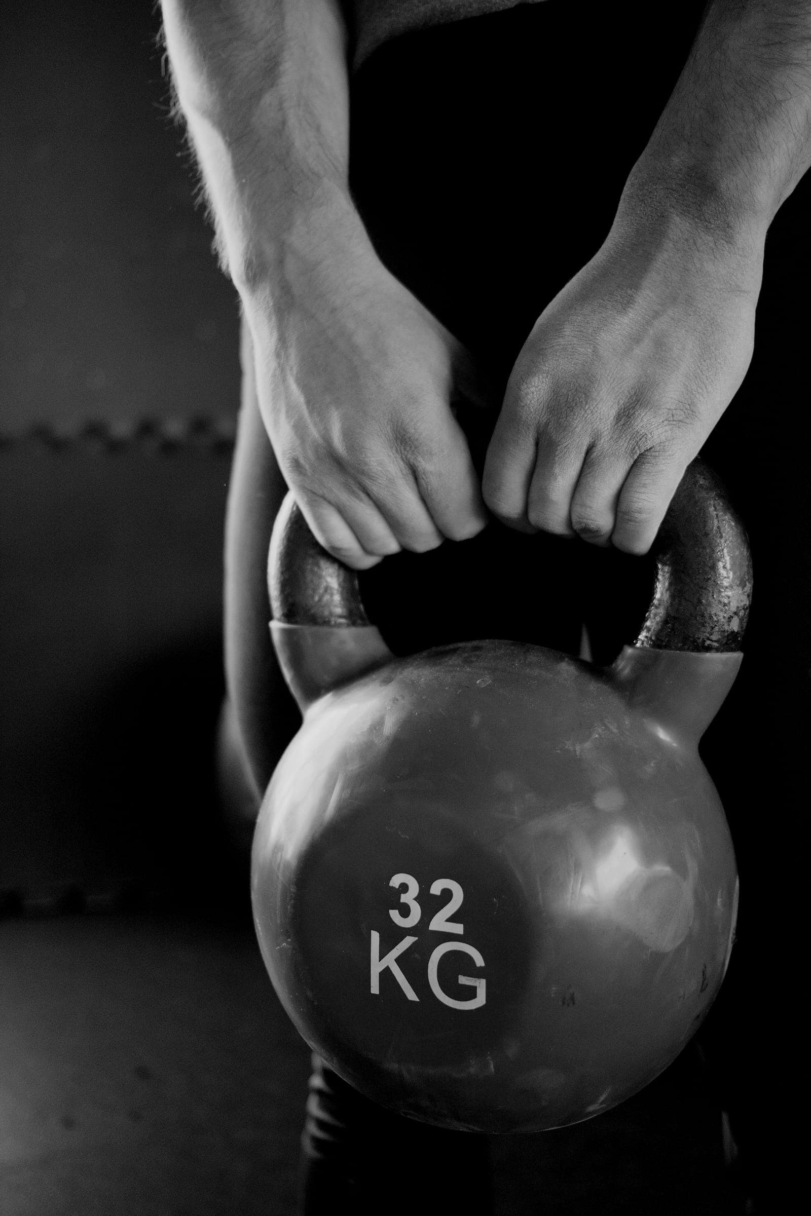 An athlete lifts a kettlebell from the floor between their feet.