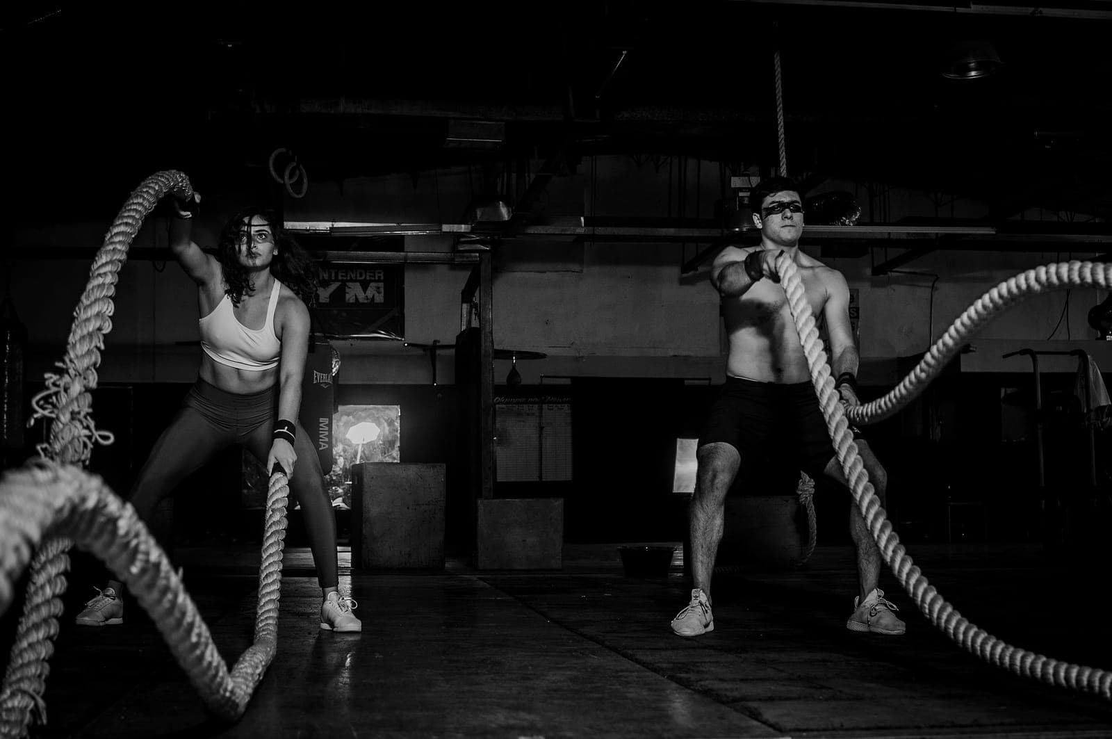 Two athletes work the battle ropes on the training floor.